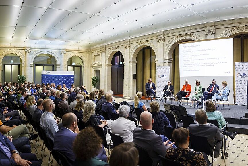 Parlamentarischer Abend des ADFC am 6. Juni 2024 Fünf personen sitzen in offenem Halbkreis auf einer Bühne und diskutieren. Im Vordergrung Publikum auf Stühlen.